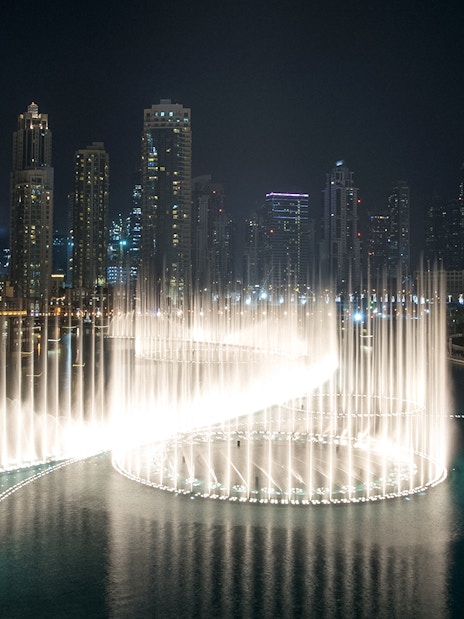 Dubai Fountain Boardwalk with illuminated water jets against city skyline at night.