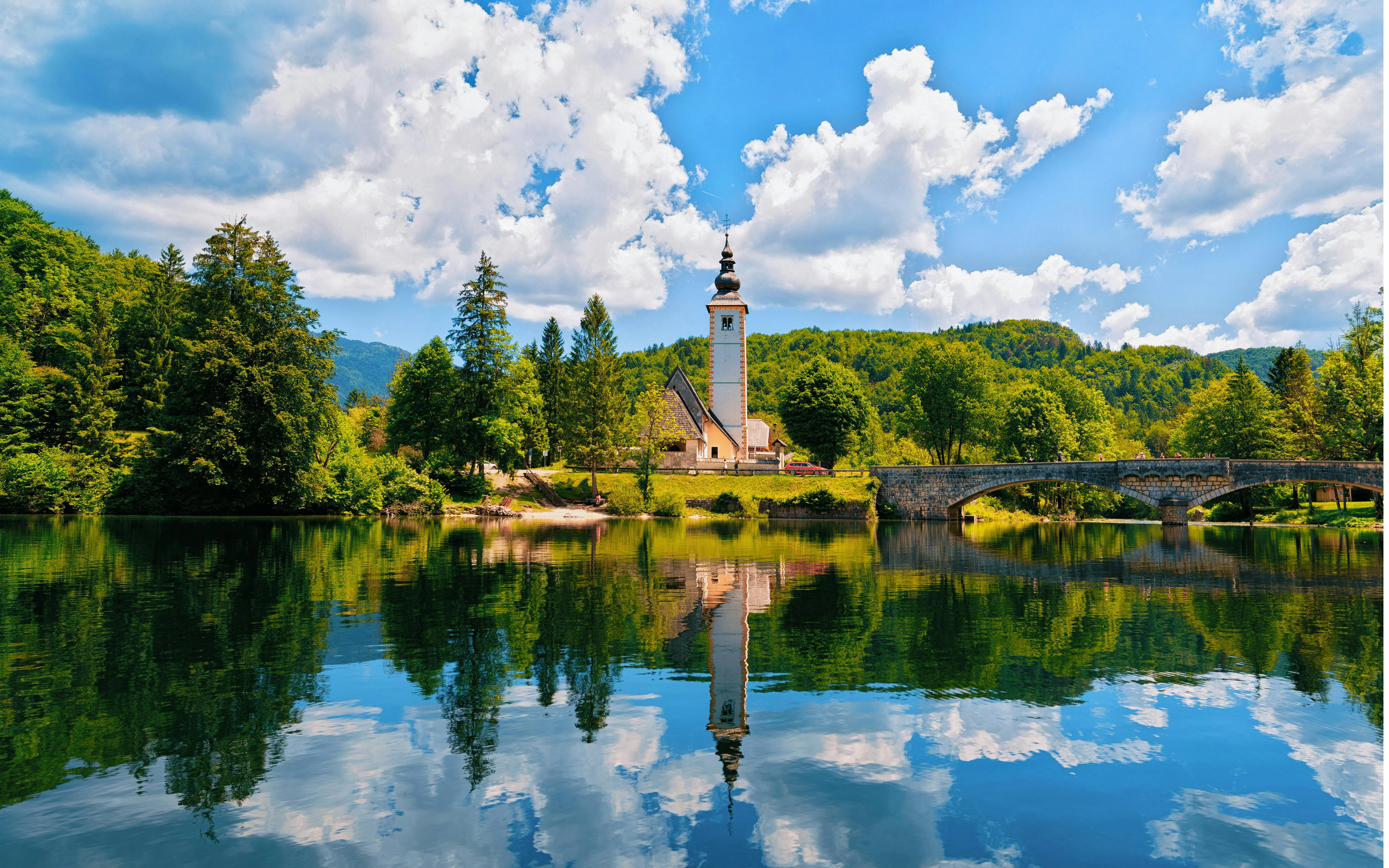 Church of St John Baptist by Bohinj Lake, Slovenia, with reflection in water and Julian Alps backdrop.