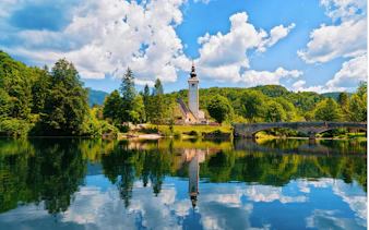 Church of St John Baptist by Bohinj Lake, Slovenia, with reflection in water and Julian Alps backdrop.