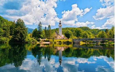 Church of St John Baptist by Bohinj Lake, Slovenia, with reflection in water and Julian Alps backdrop.