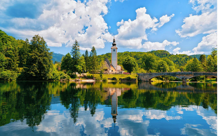 Church of St John Baptist by Bohinj Lake, Slovenia, with reflection in water and Julian Alps backdrop.