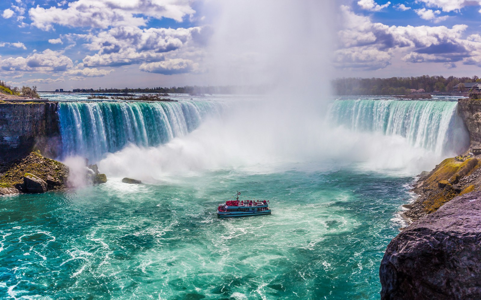 Tourist boat approaching Niagara Falls with mist rising.