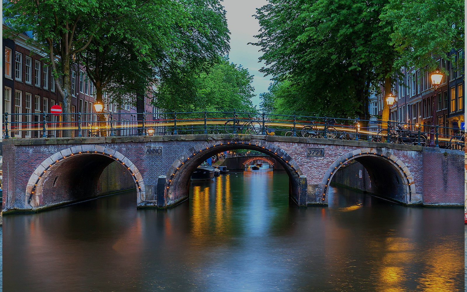 Amsterdam's illuminated canal bridge with seven arches at dusk.
