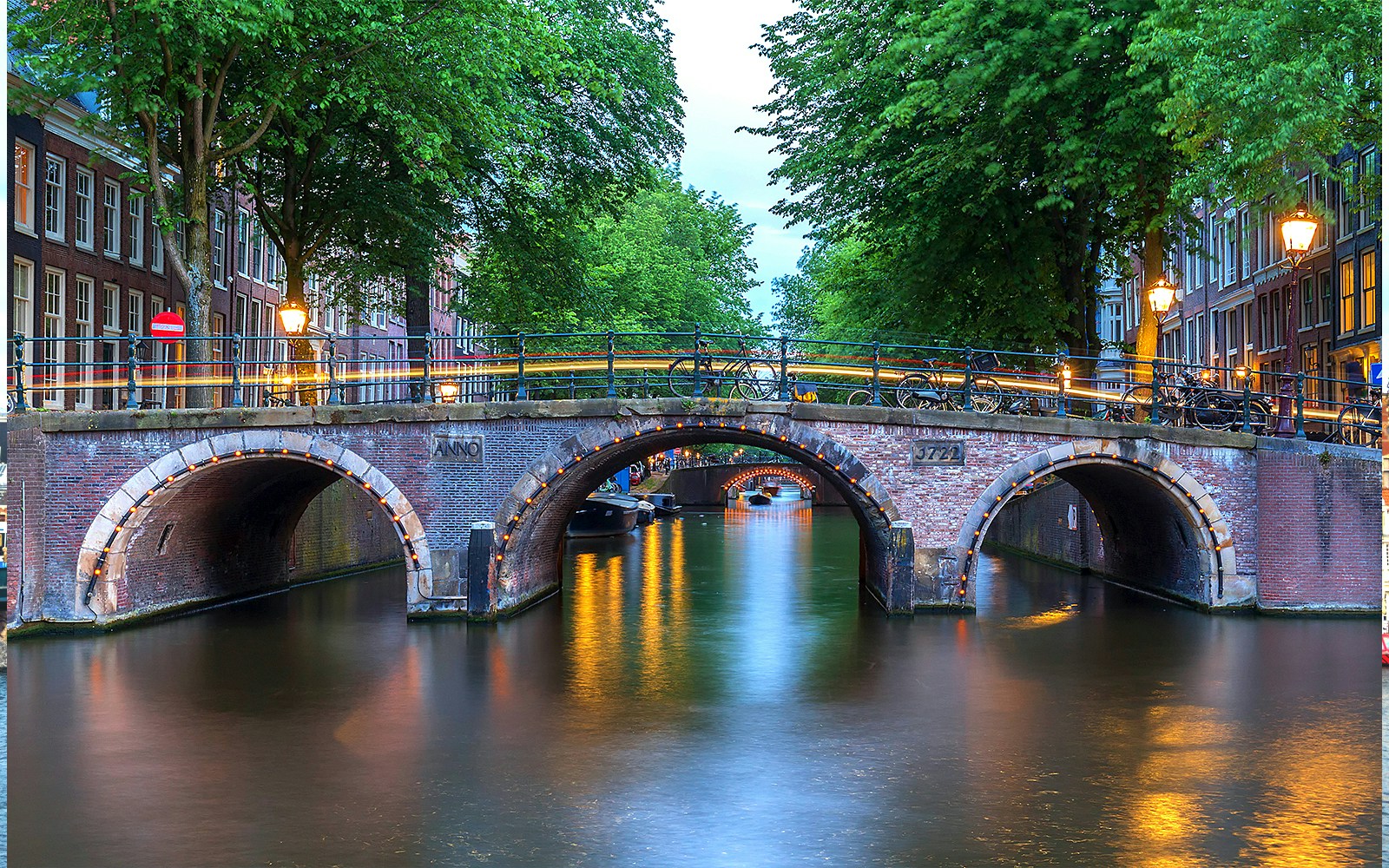 Amsterdam's illuminated canal bridge with seven arches at dusk.