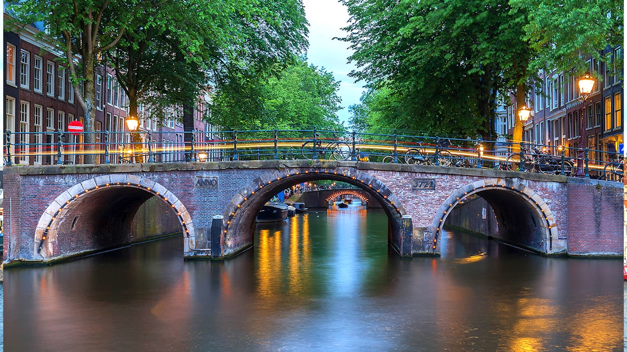 Amsterdam's illuminated canal bridge with seven arches at dusk.
