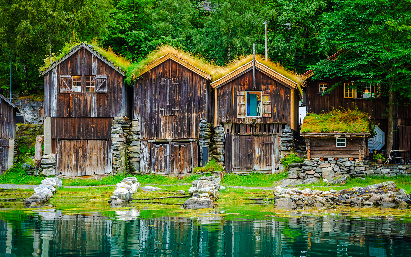 Traditional wooden houses on Geirangerfjord coast with grass roofs and stone foundations.