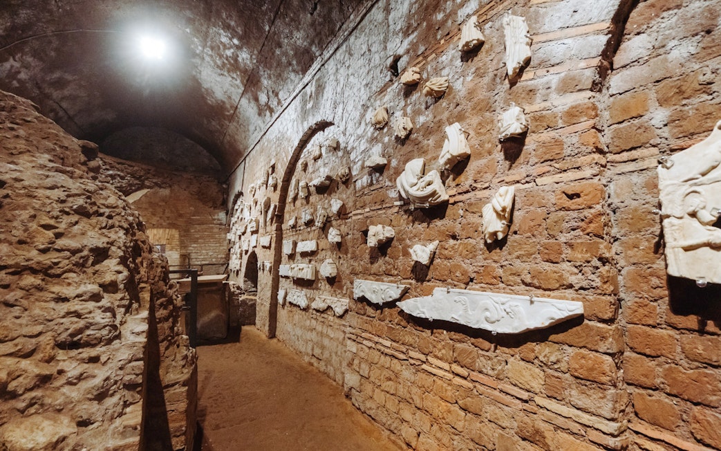 Ancient Roman catacombs with stone carvings on brick walls, part of the Underground Rome Catacombs Tour.