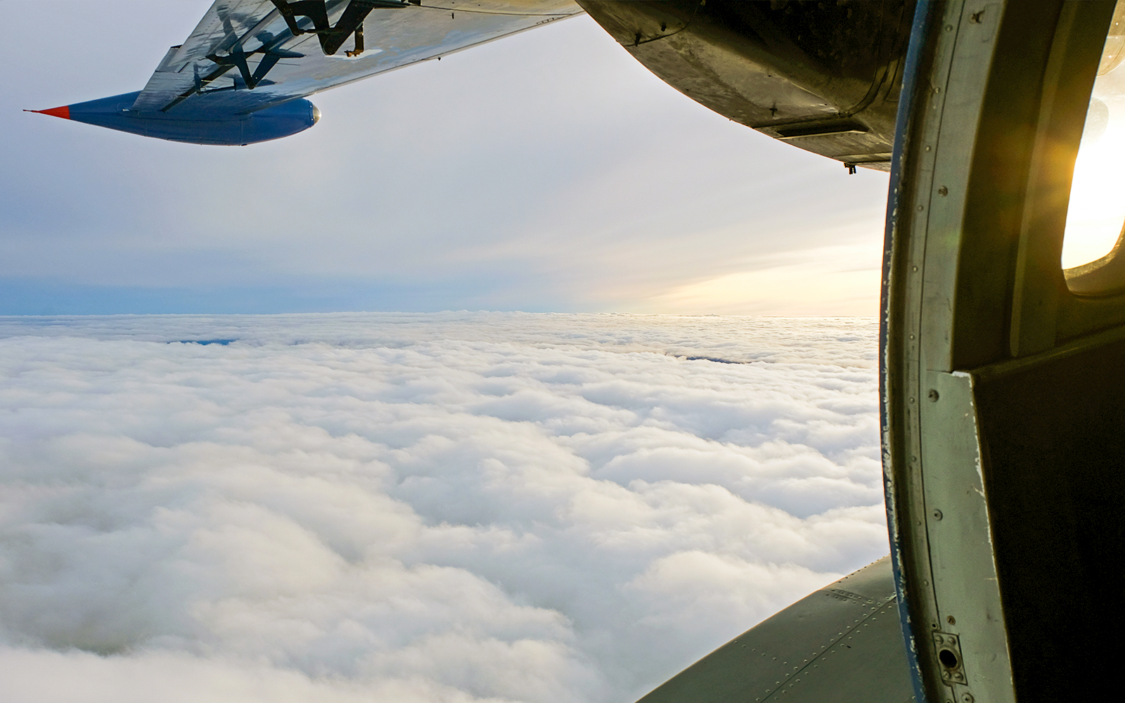 View of clouds from an open airplane door during flight.