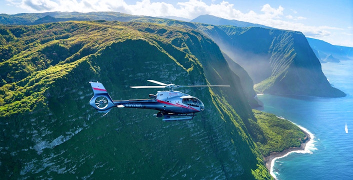 Helicopter flying over lush cliffs and ocean in Maui, Hawaii.