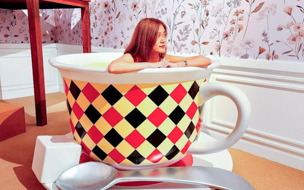 Person in a giant teacup at Alice Saves Wonderland: The Immersive Journey exhibit.