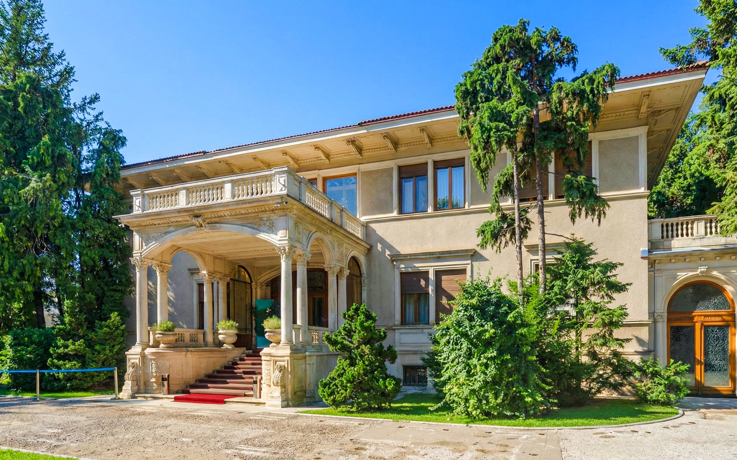 Ceausescu Mansion exterior with grand entrance and lush greenery.