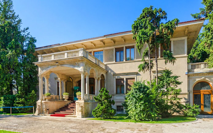 Ceausescu Mansion exterior with grand entrance and lush greenery.