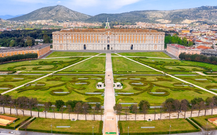 Royal Palace of Caserta with expansive gardens and mountain backdrop.