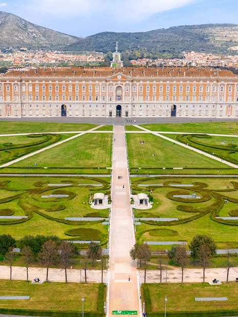 Royal Palace of Caserta with expansive gardens and mountain backdrop.