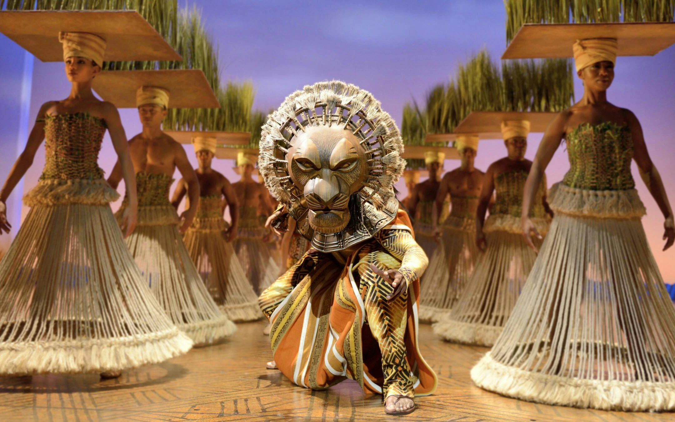 Lion King performers in traditional costumes on West End stage.