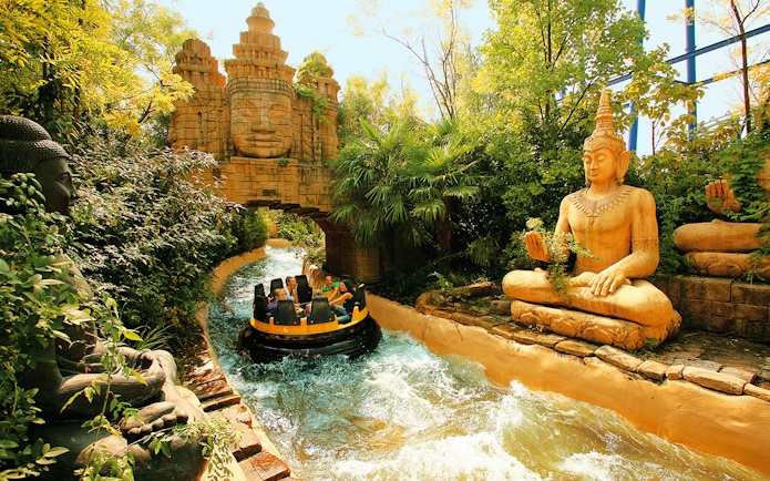 Raft on rapids passing statues and temple facade at Gardaland Park.