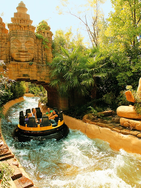 Raft on rapids passing statues and temple facade at Gardaland Park.