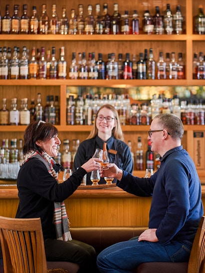 Couple toasting whisky glasses at a bar during The Gold Tour - Scotch Whisky Experience.