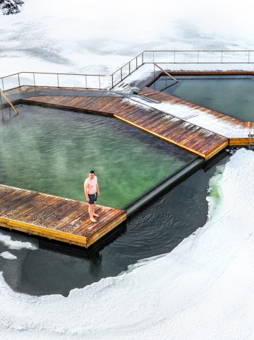 Man standing on a wooden platform at Vök Baths, surrounded by icy water in Iceland.