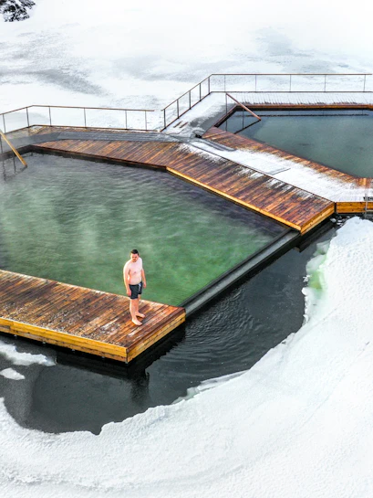 Man standing on a wooden platform at Vök Baths, surrounded by icy water in Iceland.