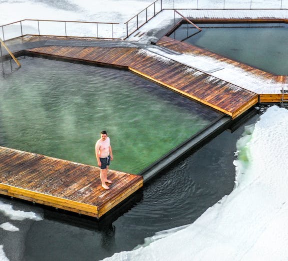 Man standing on a wooden platform at Vök Baths, surrounded by icy water in Iceland.