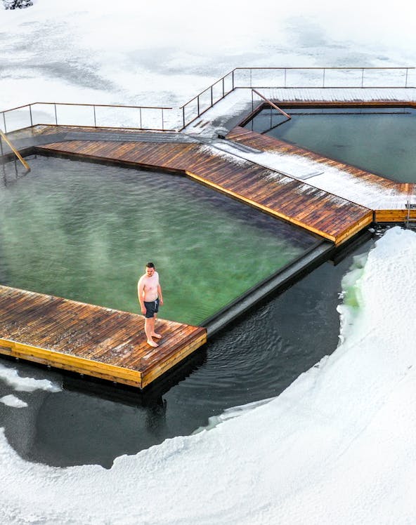 Man standing on a wooden platform at Vök Baths, surrounded by icy water in Iceland.