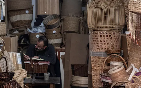 Man crafting baskets in a Colombian workshop surrounded by woven products.