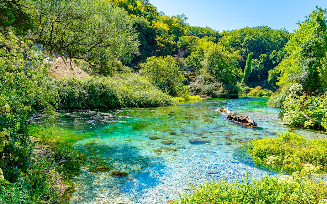 Turquoise and green water of Blue Eye Lake surrounded by lush greenery in Albania.