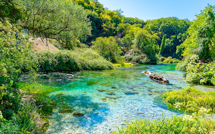 Turquoise and green water of Blue Eye Lake surrounded by lush greenery in Albania.