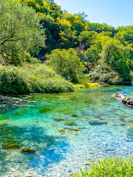 Turquoise and green water of Blue Eye Lake surrounded by lush greenery in Albania.