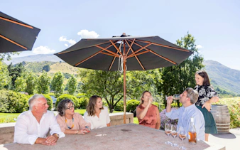 Group enjoying wine tasting under umbrellas with mountain views in Queenstown.