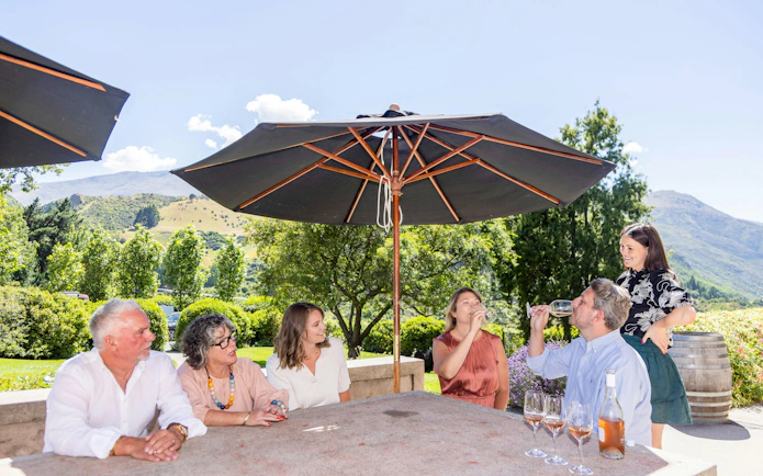 Group enjoying wine tasting under umbrellas with mountain views in Queenstown.