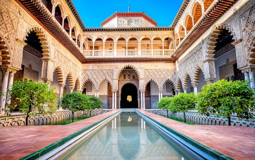 Patio de Doncellas courtyard with reflecting pool and ornate arches in Seville, Spain.