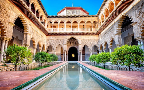 Patio de Doncellas courtyard with reflecting pool and ornate arches in Seville, Spain.