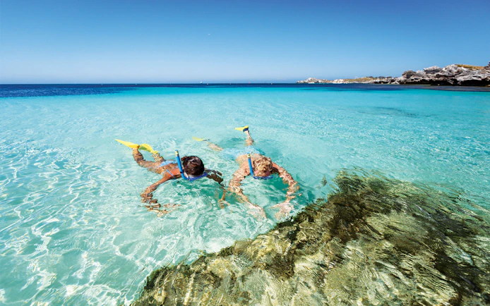 Two people snorkeling with yellow fins in clear water at Rottnest Island.