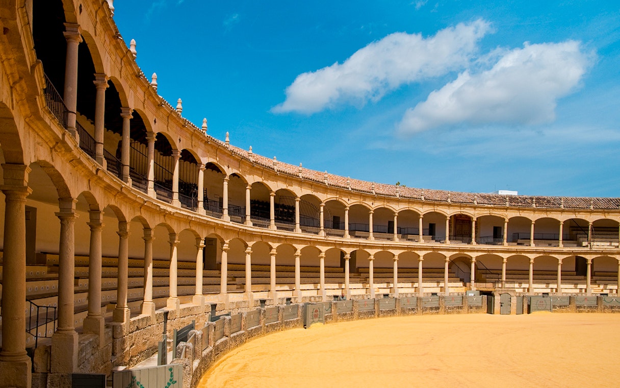 Plaza de Toros de Ronda interior with arched seating and sandy arena.