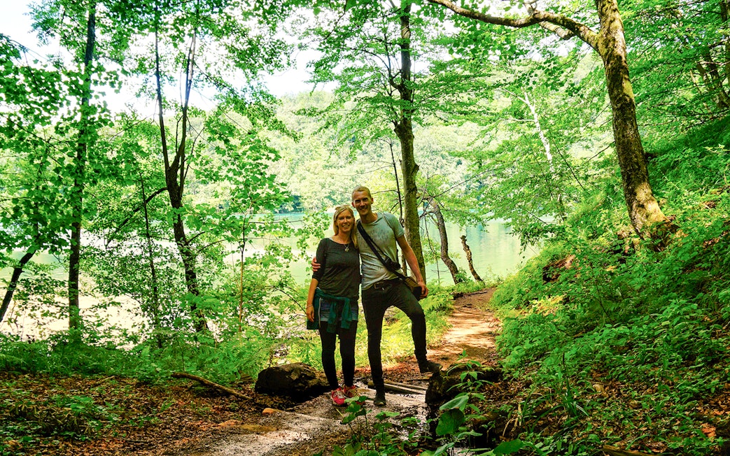 Guests walking on a forest trail by a lake in Plitvice Lakes National Park.