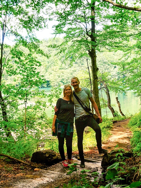 Guests walking on a forest trail by a lake in Plitvice Lakes National Park.