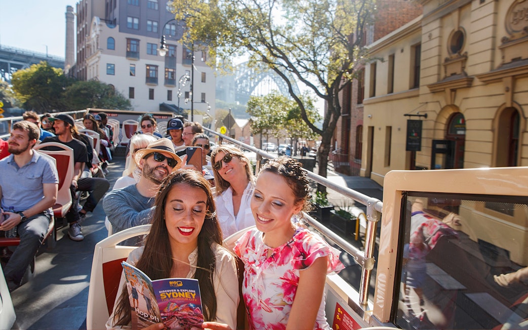 Passengers enjoying a ride on Big Bus Sydney with cityscape in the background.