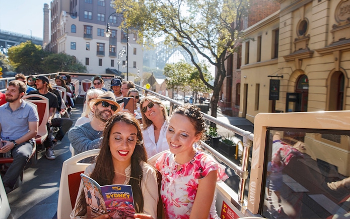 Passengers enjoying a ride on Big Bus Sydney with cityscape in the background.
