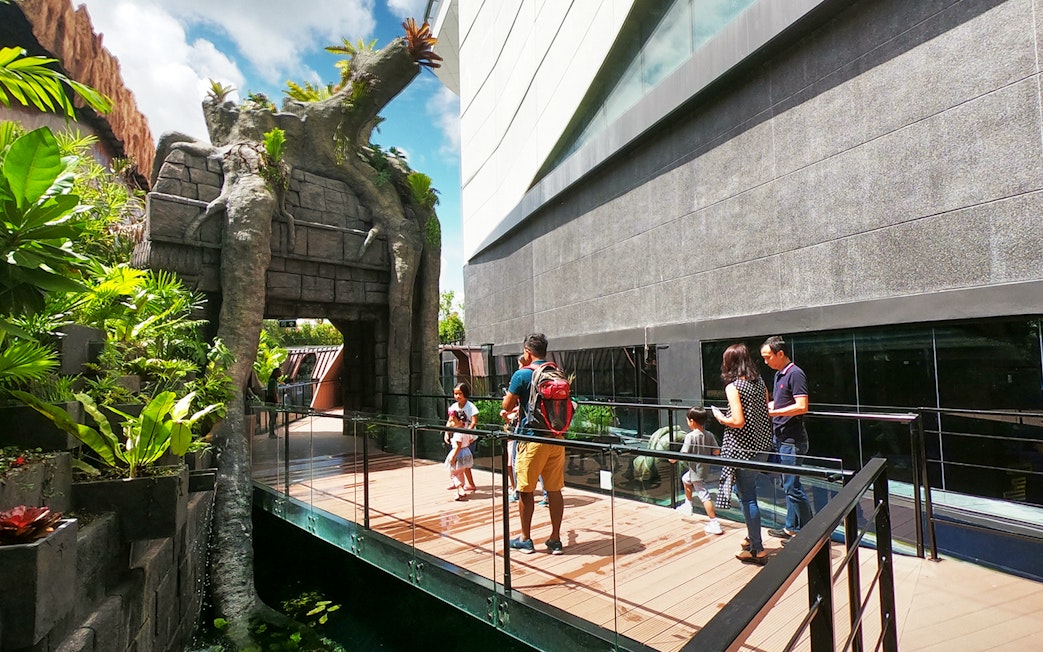 Visitors walking on a bridge at Aquaria Phuket entrance, surrounded by lush greenery.
