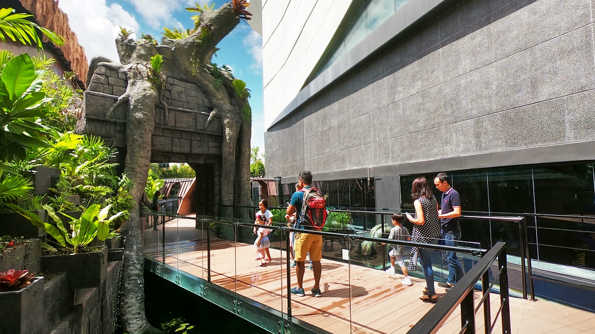 Visitors walking on a bridge at Aquaria Phuket entrance, surrounded by lush greenery.