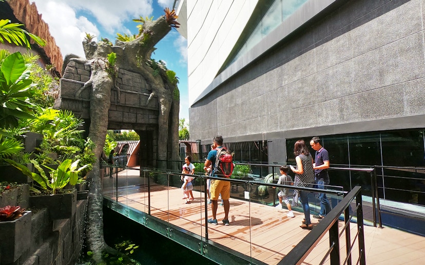 Visitors walking on a bridge at Aquaria Phuket entrance, surrounded by lush greenery.