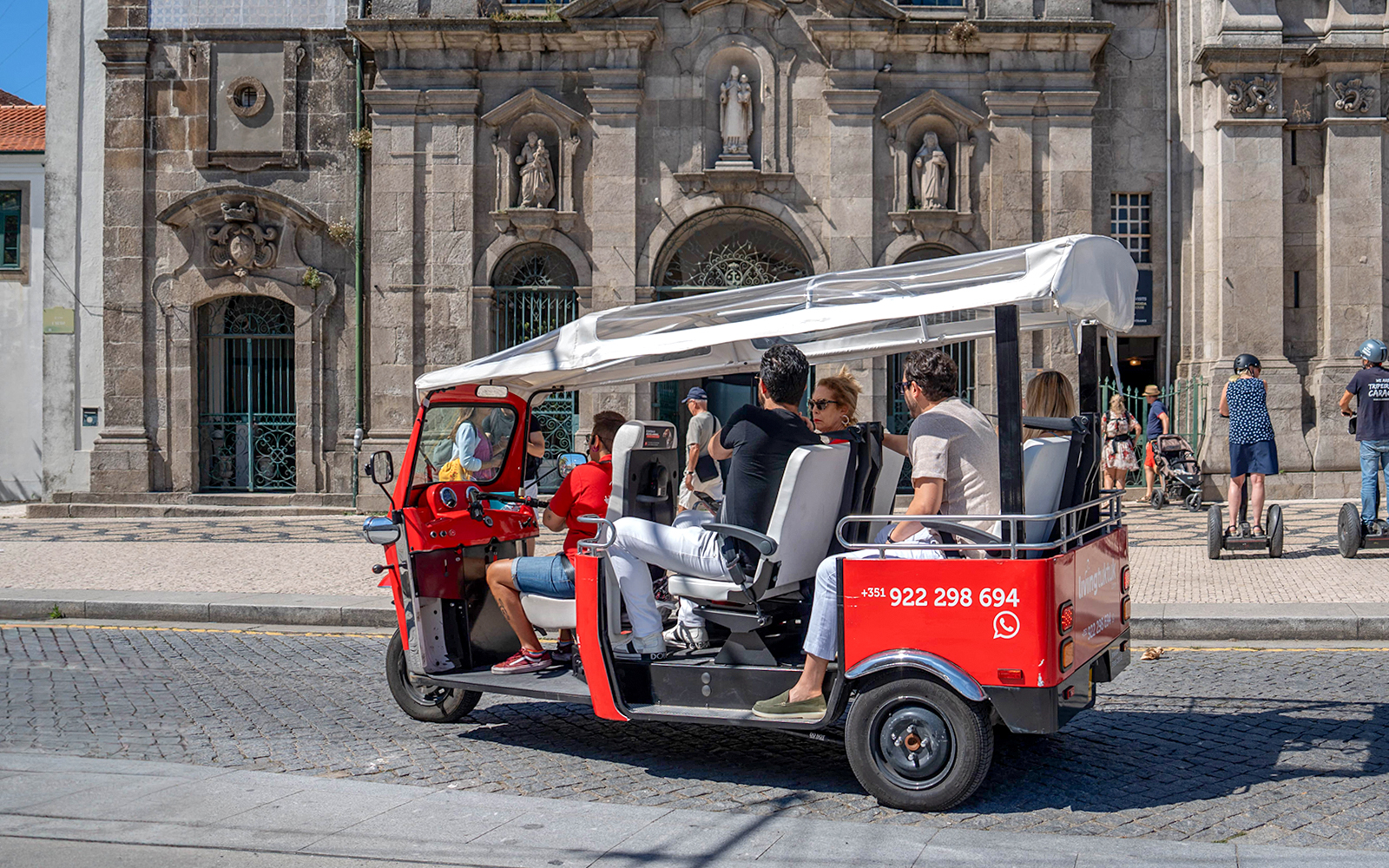 Porto electric tuk-tuk with tourists in front of historic building.