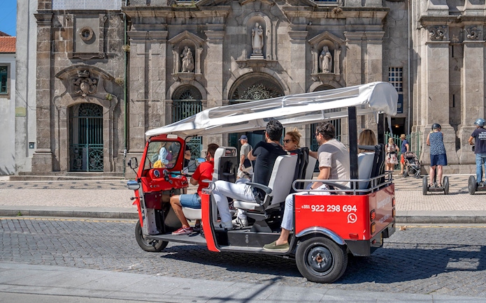 Porto electric tuk-tuk with tourists in front of historic building.
