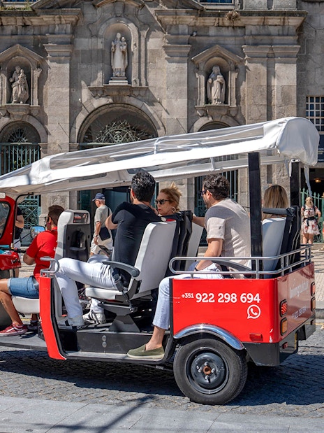 Porto electric tuk-tuk with tourists in front of historic building.