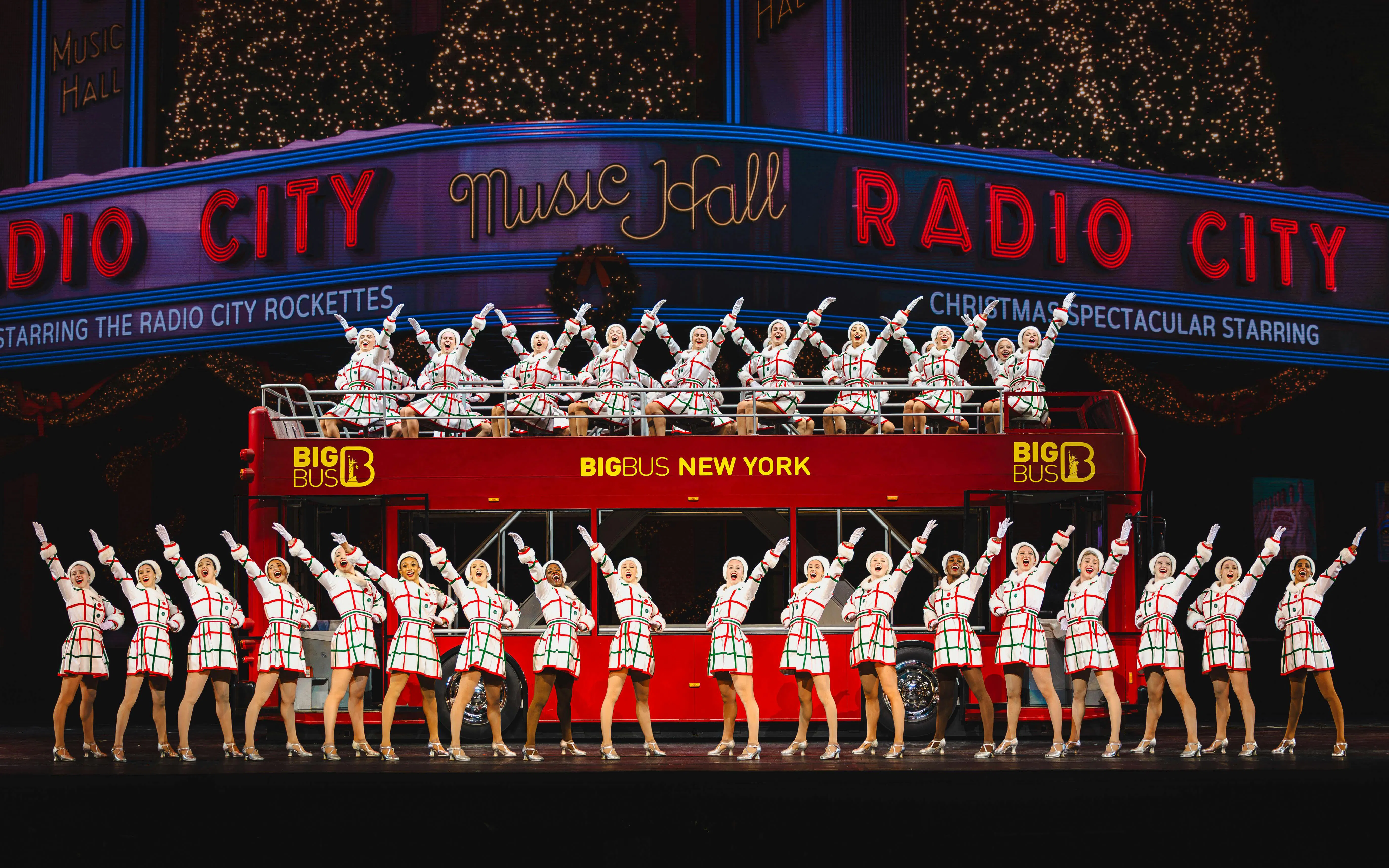 Radio City Rockettes performing on stage with a red bus backdrop in New York.