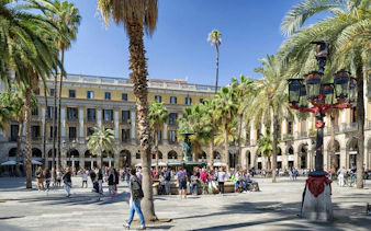 Plaza Real in Barcelona with palm trees, historic buildings, and tourists exploring the square.