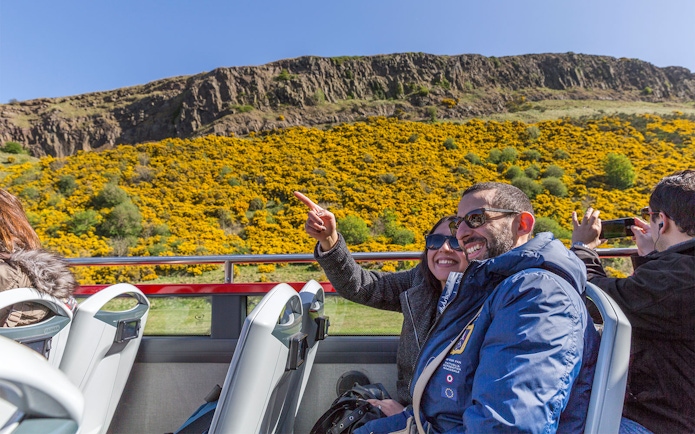 Tourists enjoying a hop-on hop-off bus tour in Edinburgh with views of Arthur's Seat.