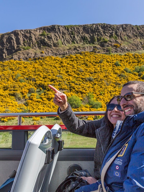 Tourists enjoying a hop-on hop-off bus tour in Edinburgh with views of Arthur's Seat.